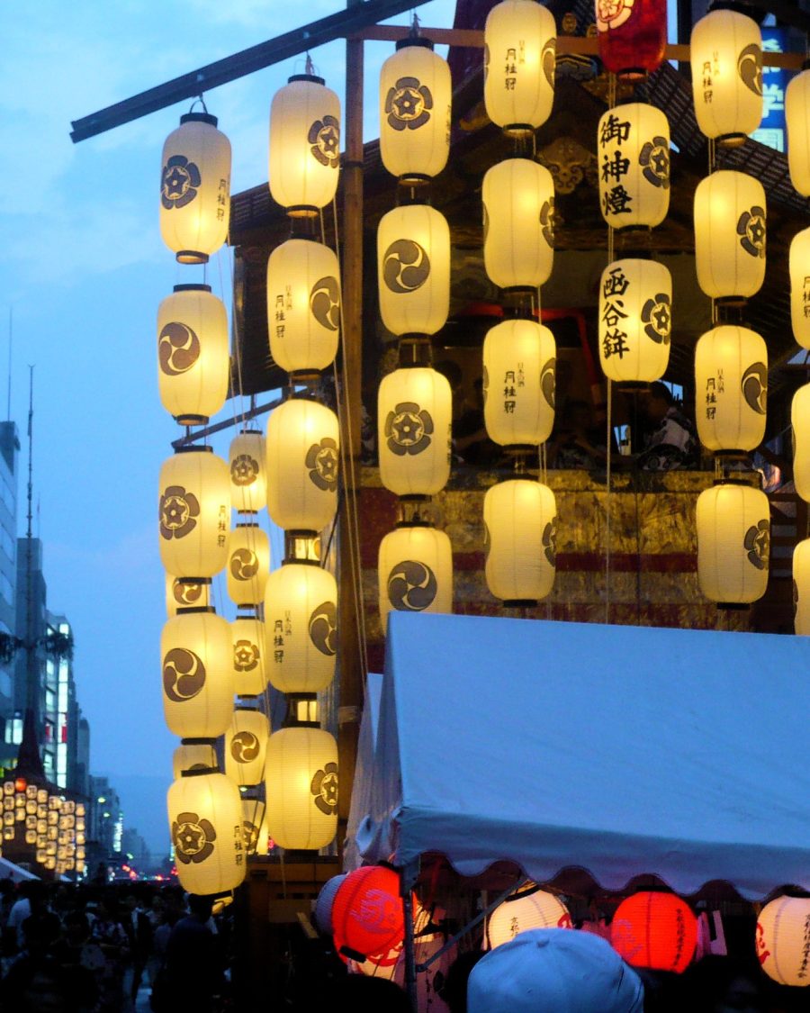 Paper lanterns strung along a festival street at night, an anime-production key-art reference