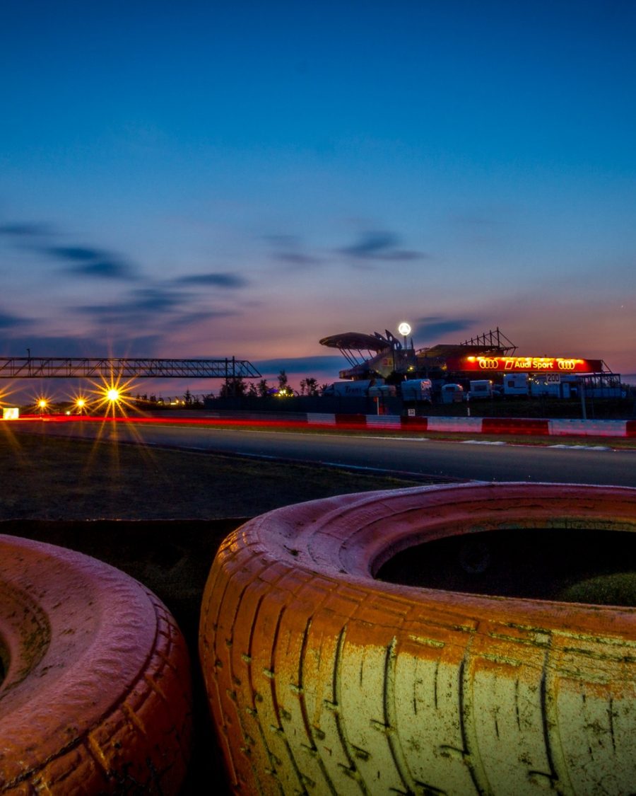 Motorsport racetrack at dusk with motion-blurred lights, an anime-production key-art reference